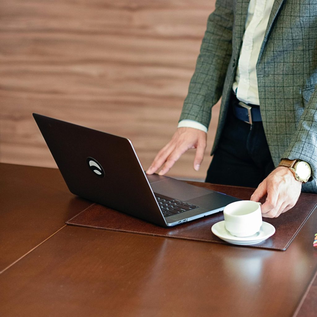 Business professional in a suit using a laptop on a wooden desk with a cup of coffee.